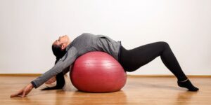 Mujer sobre una bola de gimnasio ejercitando la espalda.
