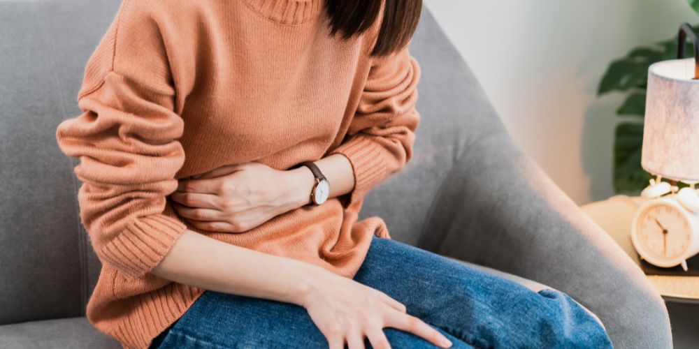 Mujer sentada en sofá con dolor de barriga.