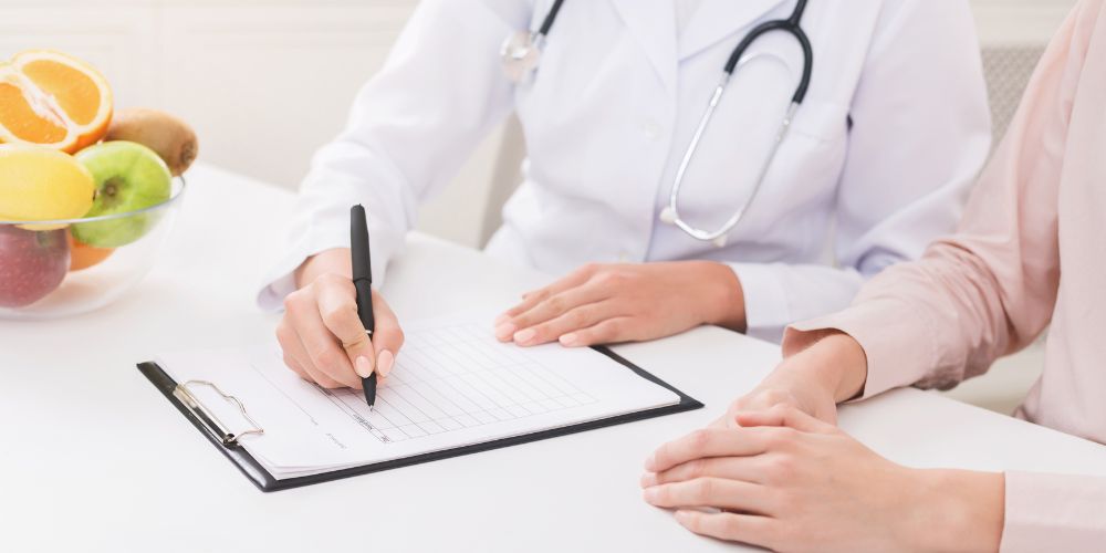 Un médico con un fonendoscopio escribiendo a un paciente que está a su derecha con un bolígrafo y un papel.