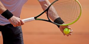 Hombre con una raqueta de tenis y una bola de tenis a punto de sacar.