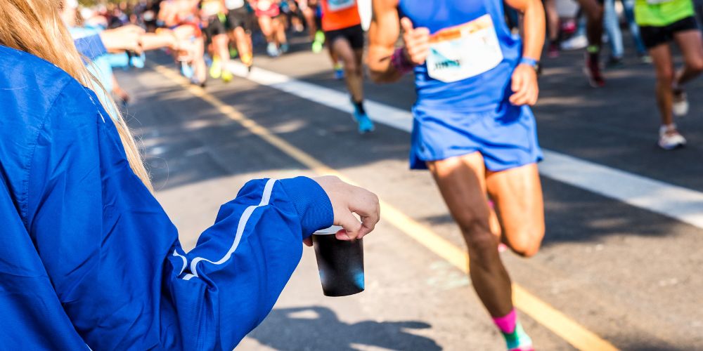 Un hombre corriendo en una maratón a punto de coger una bebida que le entregan en carrera. 