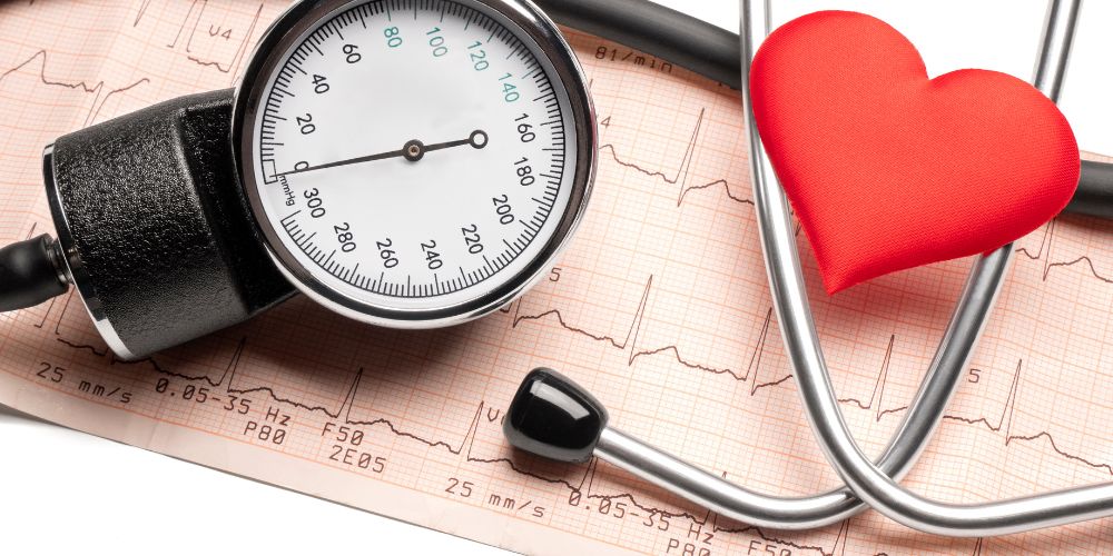 Un tensiómetro manual con un corazón rojo al lado. Debajo hay un gráfico de papel de un electrocardiograma.