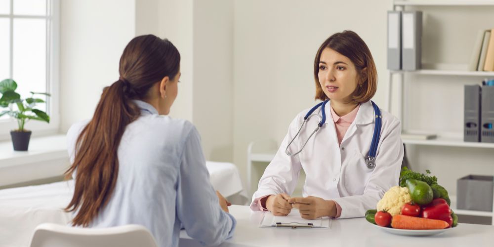 Una médico y una mujer sentadas. En el medio hay una mesa y un plato con fruta.