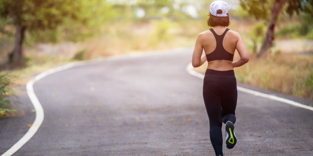 Mujer de espaldas corriendo por una carretera sin coches.