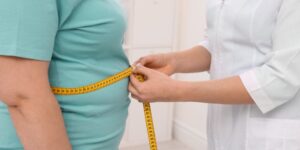 Un médico tomándole la medida de la barriga a un hombre con una cinta.