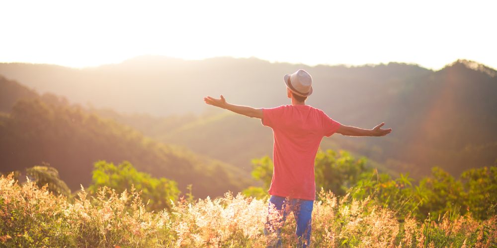 Un hombre al aire libre en una montaña con los brazos abiertos y un gorro en la cabeza.