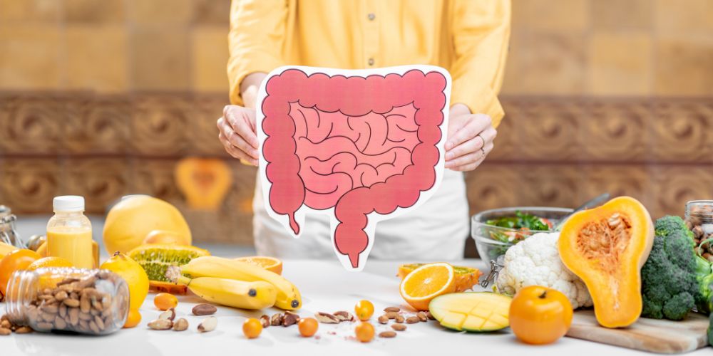 Una mujer enseñando el dibujo de unos intestinos en una cocina con frutas en la mesa.