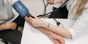 Mujer médico sentada tomando la tensión con un tensiómetro a un paciente que está sentado.