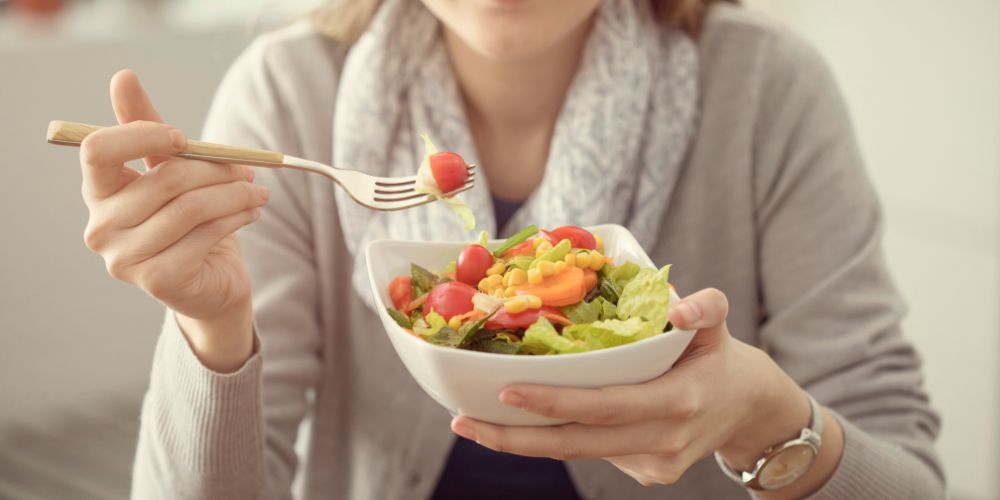 Mujer sujetando una ensalada y un tenedor en sus manos.