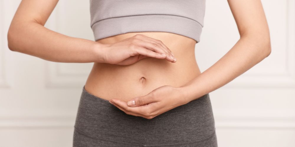 Mujer con una mano encima y otra debajo de su barriga. Entre las manos está el ombligo.