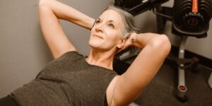 Mujer de mediana edad acostada en un gimnasio haciendo ejercicios.