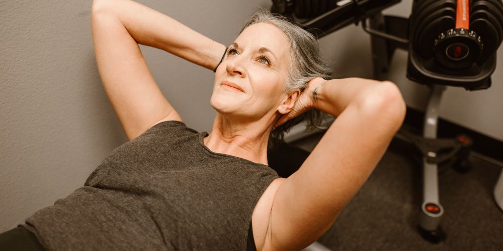 Mujer de mediana edad acostada en un gimnasio haciendo ejercicios.