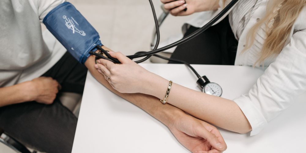 Mujer médico sentada tomando la tensión con un tensiómetro a un paciente que está sentado.