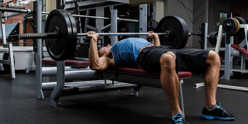 Hombre en el gimnasio acostado levantando una pesa sobre el pecho.