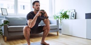 Hombre levantando peso en casa con una pesa.