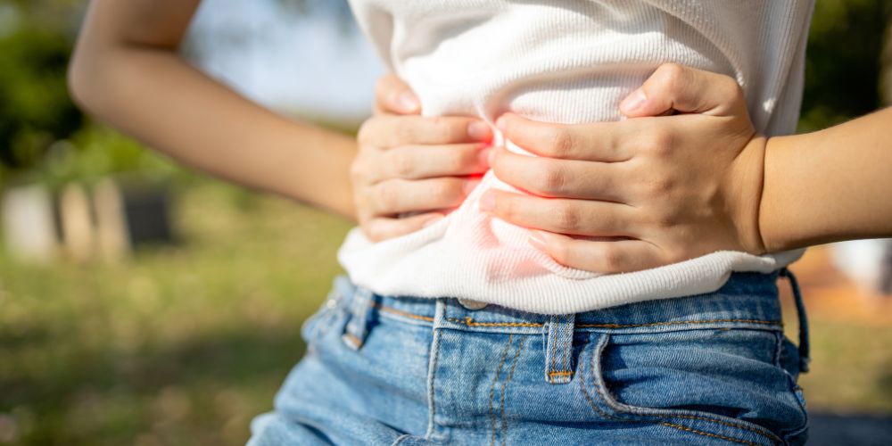 Mujer agarrándose la barriga con las dos manos con dolor.