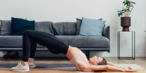 Mujer haciendo ejercicio en casa sobre una esterilla. Tiene las piernas, la cabeza y los brazos apoyados en el suelo. El tronco está levantado.