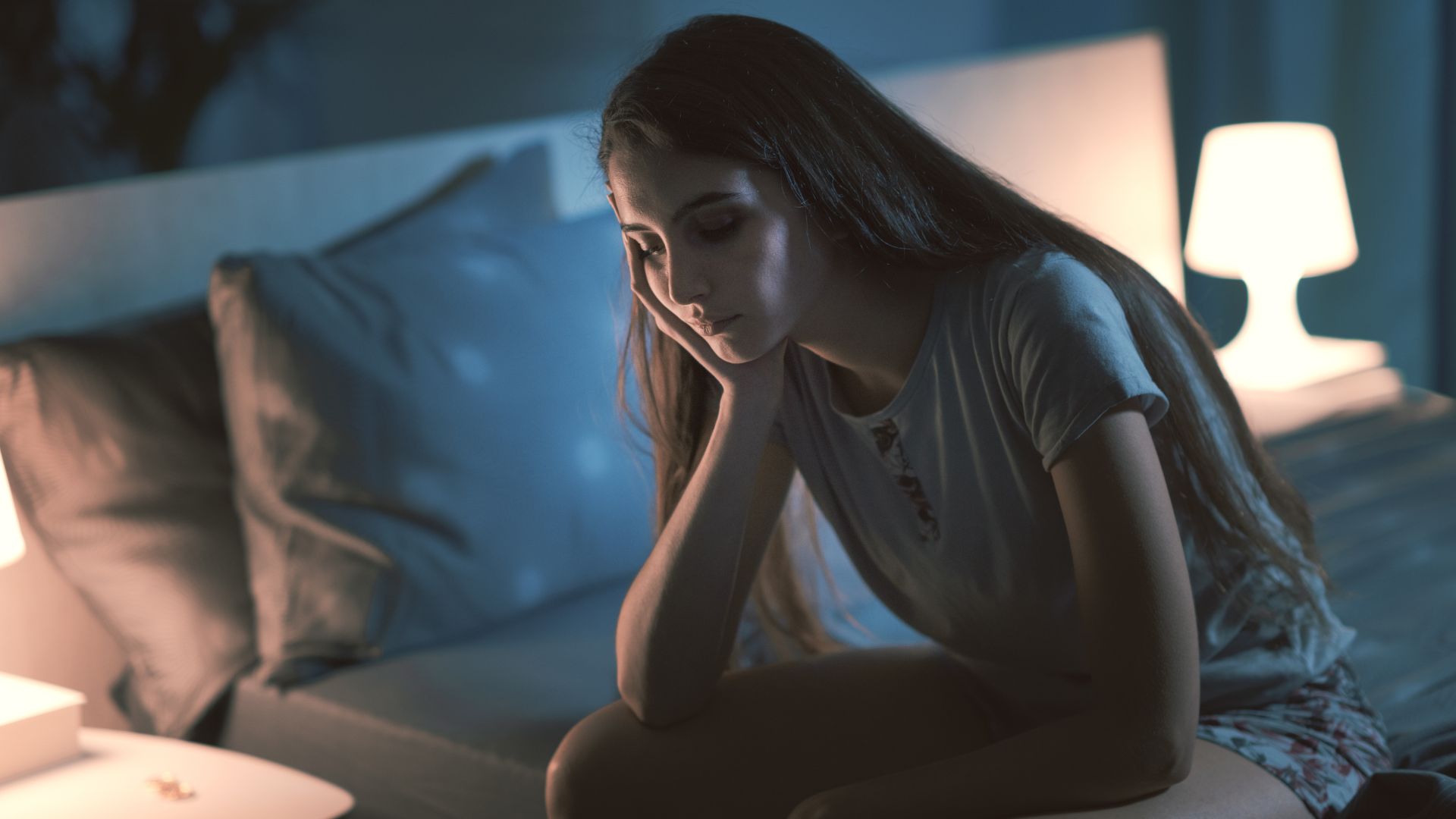 mujer joven sobre una cama con cara de preocupación