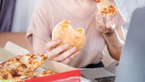 una persona comiendo pizza y hamburguesa mientras mira un ordenador
