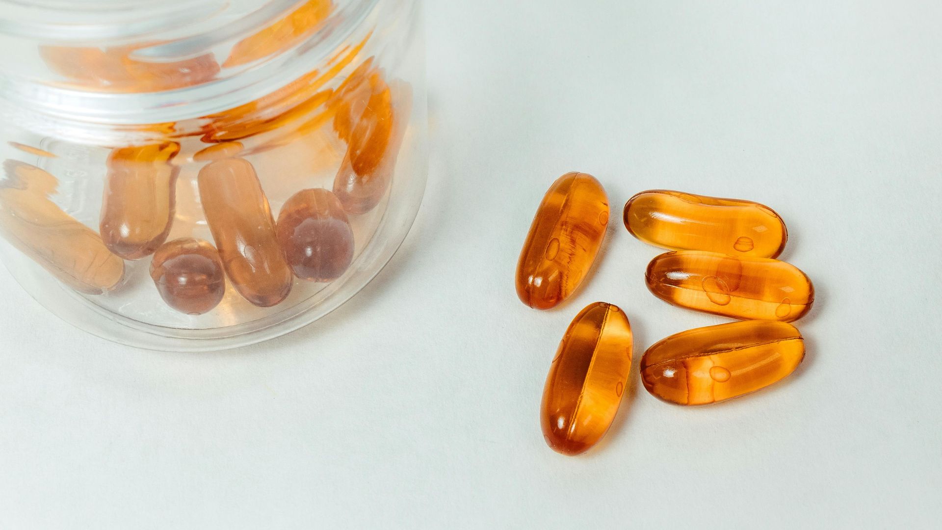Imagen de una superficie con un bote de cristal lleno de pastillas y 5 pastillas en la mesa