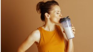 mujer con camiseta naranja bebiendo un batido de proteina