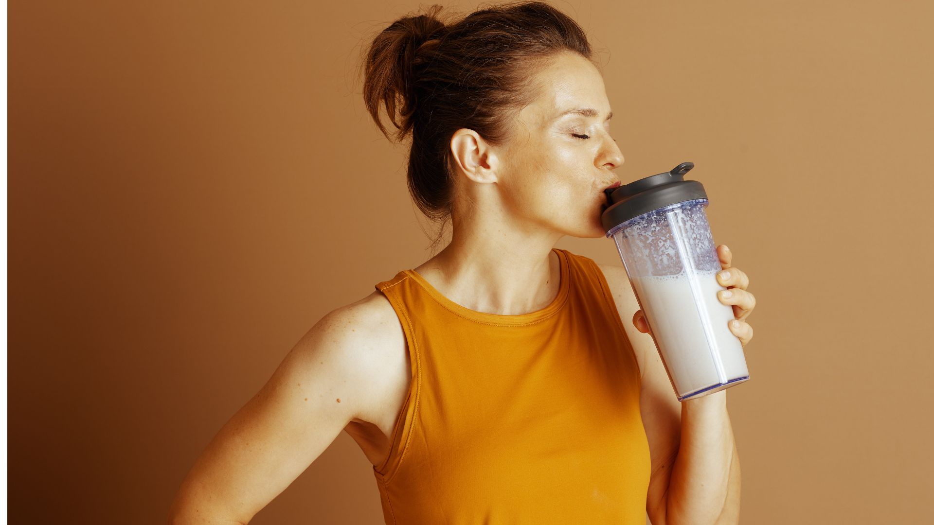 mujer con camiseta naranja bebiendo un batido de proteina