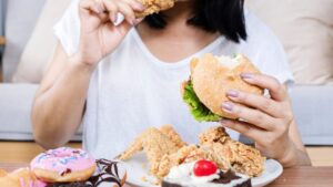 mujer en una mesa con un plato de donuts, pollo frito y comiendo pollo frito y en la otra mano hamburguesa
