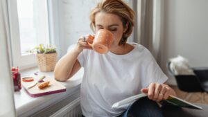 Mujer comiendo un croissant con mermelada ,mientras lee y se toma un café